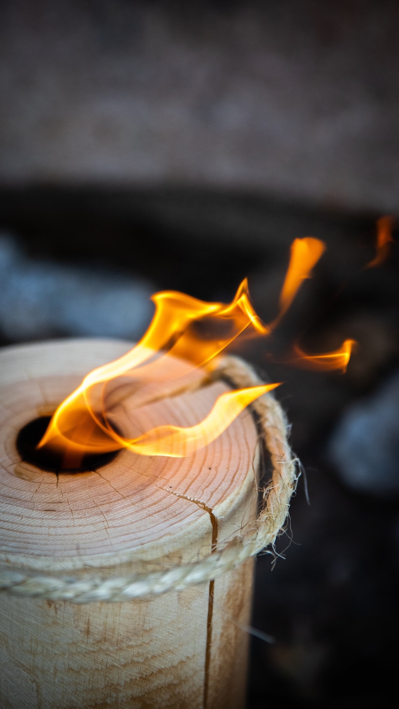May include: A wooden log with rope wrapped around it, burning with a bright orange flame in the centre.