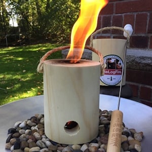 May include: A wooden log fire pit with a flame burning inside. The fire pit is surrounded by small stones and a wooden stick with the text "One Log Fire" is on the ground.
