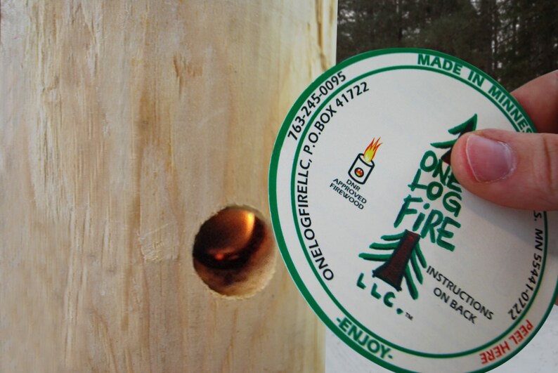 May include: A white round sticker with green text and a green pine tree design. The text reads "One Log Fire LLC. Made in Minnesota. 763-245-0095 P.O. Box 41722 S. MN 55441-0722 DNR Approved Firewood Instructions on Back -Enjoy- Peel Here".