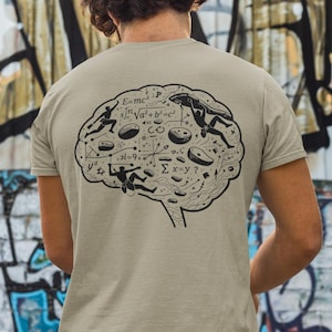Può includere: T-shirt beige con un disegno nero di un cervello pieno di simboli e figure matematiche. Il disegno del cervello include omini stilizzati che interagiscono con le equazioni. La maglietta è realizzata in materiale morbido.