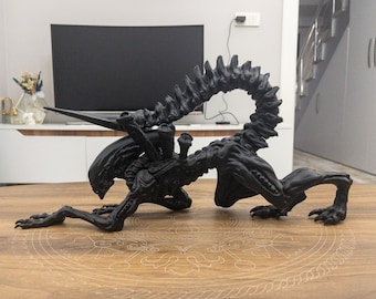 Puede incluir: Una figura de criatura alienígena negra impresa en 3D con una cola larga y dientes afilados. La figura está en posición de arrastre con la cabeza baja.