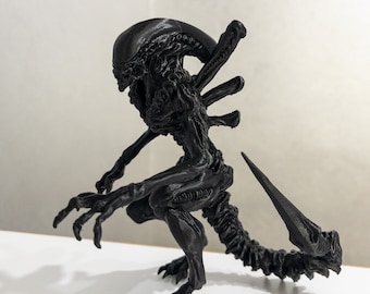 Puede incluir: Una figura negra de una criatura extraterrestre impresa en 3D con una cola larga y garras afiladas. La criatura está en posición de cuclillas con la cabeza inclinada hacia abajo.