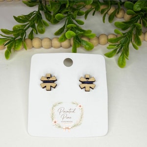 May include: Wooden stud earrings with a geometric design and a dark blue stripe. The earrings are displayed on a white card with the text "Painted Pine Handmade" in a floral wreath.