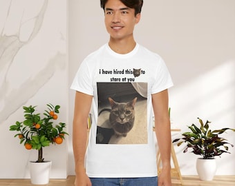 Pode incluir: Camiseta branca com um gráfico de um gato cinza e o texto "i have hired this to stare at you". O gato está olhando diretamente para o espectador. A camiseta está sendo usada por uma pessoa.