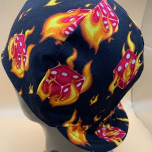 May include: Black welding cap with a pattern of red dice on fire. The dice are outlined in white and the flames are yellow.