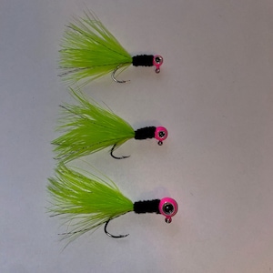 May include: Three lime green jig heads with black and pink accents. The jig heads have a feathered body and a hook.