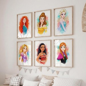 May include: Set of six framed watercolor prints featuring Disney princesses. Each portrait showcases a different princess with vibrant colors and a watercolor effect. The frames are a light wood color, and the prints are displayed on a white wall.