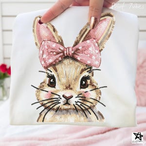 May include: White t-shirt with a sequined bunny face, pink bow, and ears. The bunny has brown eyes, whiskers, and rosy cheeks. The text "Print 7vibes" is in the upper right corner.