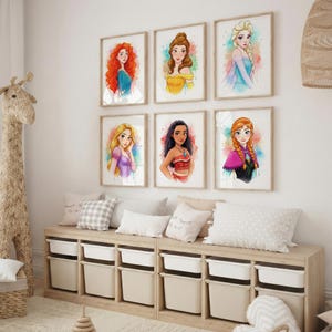 May include: Six framed watercolor prints of Disney princesses hang on a white wall. The artwork features vibrant colors and depicts characters like Elsa, Belle, and Ariel. Below, a wooden storage unit with white bins and decorative pillows.