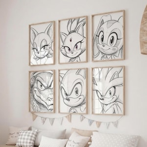 Puede incluir: Seis impresiones artísticas enmarcadas a lápiz con personajes de la franquicia Sonic the Hedgehog. La obra de arte es en blanco y negro, con el retrato de cada personaje en un marco de madera. Las impresiones se muestran sobre una cama.
