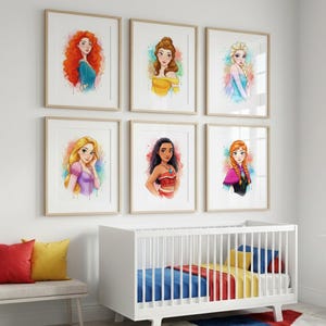 May include: Six framed watercolor prints of Disney princesses, including Merida, Belle, Elsa, Rapunzel, Moana, and Anna. Each portrait features vibrant colors and is set against a white background. The prints are displayed above a white crib and a bench with colorful pillows.