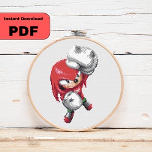 May include: A cross-stitch embroidery hoop with a pixelated image of Knuckles the Echidna from the Sonic the Hedgehog series. The character is in red, white, grey, and green. The text "Instant Download PDF" is in a red rectangle.