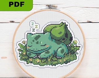 以下が含まれることがあります： 木製の刺繍枠に入ったクロスステッチパターン。背中に球根を乗せた緑色の生き物が、小さな黄色い花が咲く草むらで眠っているピクセルアートのイラストで、吹き出しにはZの文字が3回繰り返されています。