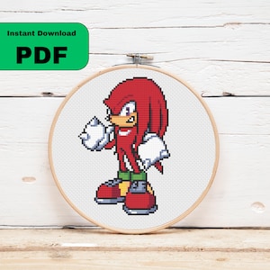 May include: A cross-stitch pattern of Knuckles the Echidna in a wooden embroidery hoop. The character is red with white gloves and shoes, green shorts, and a yellow buckle. The words "Instant Download PDF" are in a green rectangle.