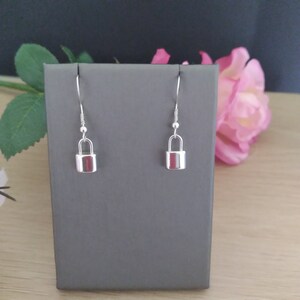 May include: A pair of silver padlock dangle earrings. The earrings are displayed on a gray stand.