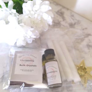 May include: A collection of spiritual items including a bottle of Crossing Oil, a packet of Uncrossing Bath Crystals, white candles, and a gold star-shaped decoration. White flowers are in the background.