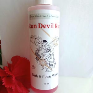 May include: A clear bottle of "Run Devil Run" bath and floor wash. The label features an illustration of an angel and the text "Bath & Floor Wash" and "8 oz". The liquid inside is pink, and the bottle has a white cap.