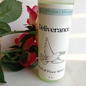 May include: A clear bottle of "Deliverance" bath and floor wash with a white label featuring a dove carrying an olive branch. The bottle is 8 oz and has a light green liquid inside. The words "Rose Blossoms Naturals" are at the top.
