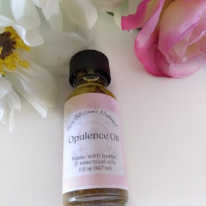 May include: A small glass bottle with a black cap, filled with a green liquid. The label is pink and white with the text "Rose Blossoms Natural Opulence Oil Made with herbs & essential oils 1/2 oz (14.7 ml)"