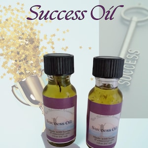 May include: Two small glass bottles with black caps filled with a clear liquid and labeled "Success Oil". The bottles are made with herbs and essential oils. The bottles are sitting on a white surface with a gold trophy and a silver key in the background.
