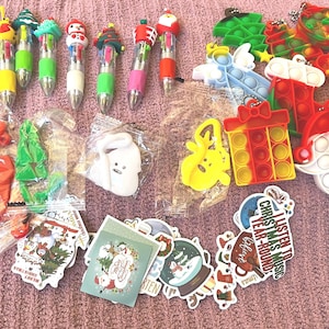 May include: A collection of holiday-themed items including seven multi-color ink pens with festive toppers, several silicone bubble fidget toys in shapes like Santa, trees, and gifts, and a variety of Christmas-themed stickers with text.