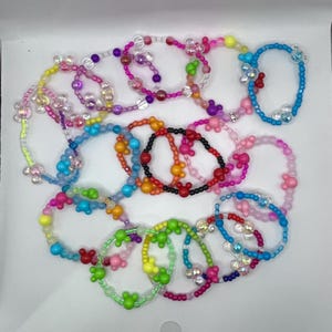 May include: A collection of colorful beaded bracelets. The bracelets feature various colors, including pink, blue, green, and yellow, with Mickey Mouse-shaped beads and other decorative elements. The beads are strung together to form a circular shape.