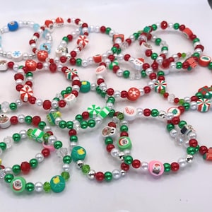 May include: A collection of circular bracelets made from small red, green, and white beads. Each bracelet features various holiday-themed charms, including miniature Santa Claus faces, reindeer, candy canes, snowflakes, and wrapped gift boxes.