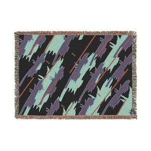 May include: A rectangular throw blanket with a black background and a repeating pattern of diagonal shapes in teal, purple, and orange. The blanket has a fringed edge.