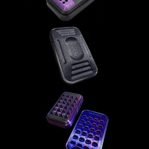 May include: A series of rectangular, 3D-printed cases in black and purple. The top case has a lid with a grid of holes and a central square. The middle case is solid with a recessed area. The bottom cases have patterned surfaces.