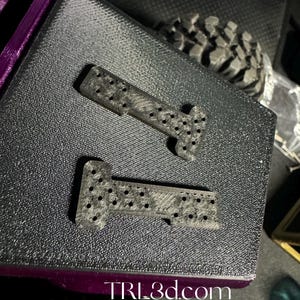 Puede incluir: Dos piezas de plástico negro con una superficie texturizada y pequeños agujeros. Las piezas tienen forma de T e I. El texto "TRL3d.com" es visible en la esquina inferior derecha de la imagen.