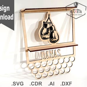 Op de afbeelding: Een houten wandplank met een bokshandschoenontwerp en de naam "DANAS" gegraveerd op de voorkant. De plank heeft een reeks gaten om spullen in te bewaren.