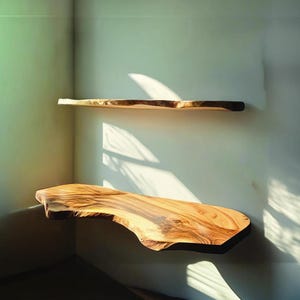 Puede incluir: Dos estantes flotantes de madera con bordes naturales están montados en una pared de color claro. Los estantes están hechos de madera natural, mostrando la veta y la textura. El estante superior es más estrecho que el inferior. La luz del sol proyecta sombras en la pared.