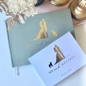 Op de afbeelding: Twee gastenboeken voor bruiloften met gouden accenten. Het groene boek heeft een silhouet van een stel en een hond. Het witte boek heeft een silhouet van een stel en een hond met de tekst "MR and MRS FREE 26.02.2022".