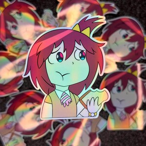 May include: A sticker featuring a cartoon girl with red hair, wearing a yellow bow and a light brown shirt. She is holding a sandwich in her right hand and has a worried expression on her face. The sticker has a holographic finish.