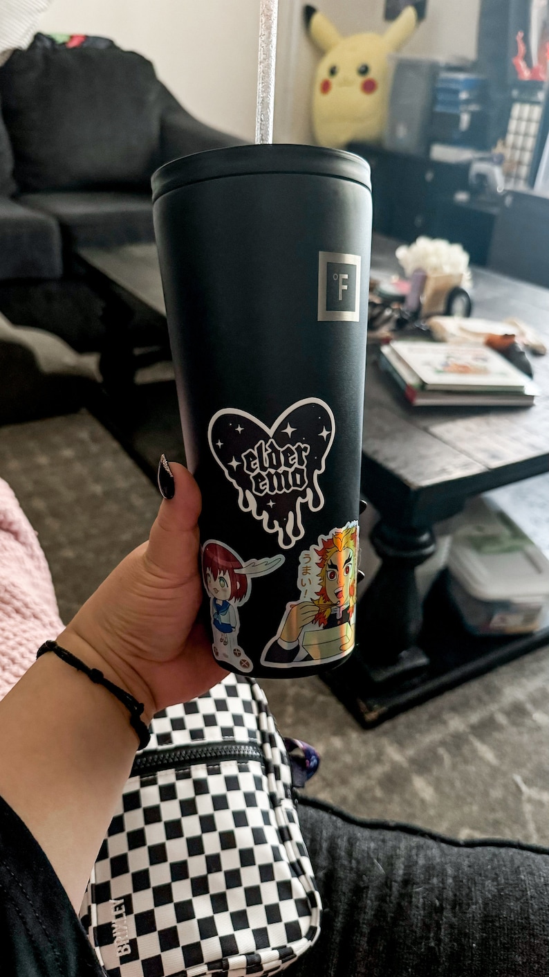 May include: A black stainless steel tumbler with a clear plastic straw. The tumbler has a sticker of a heart with the words "elder emo" on it. There are other stickers on the tumbler, including one of a cartoon character.