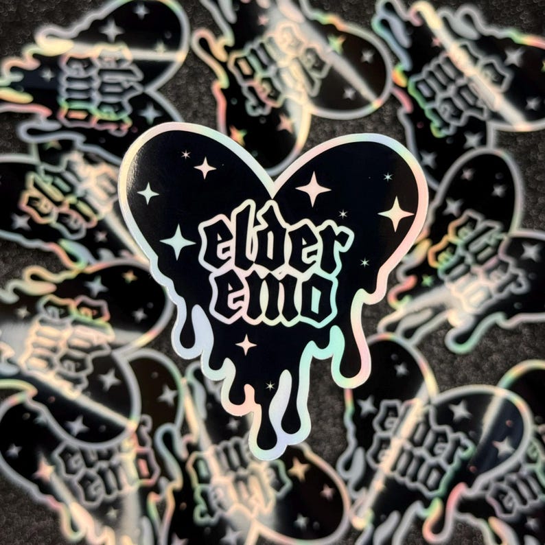 May include: A holographic sticker with a dripping black heart shape. The heart has the text "elder emo" in a gothic font and stars inside.
