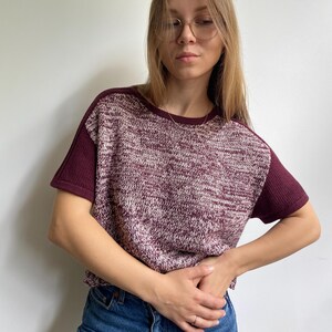 May include: A burgundy and white knit t-shirt with short sleeves. The sleeves and neckline are a solid burgundy colour. The shirt is paired with blue jeans.