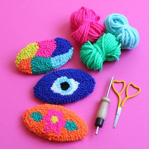 May include: A set of colorful yarn balls, a needle tool, and three colorful oval-shaped punch needle embroidery pieces. The embroidery pieces are a blue eye, a multi-colored design, and a flower design.