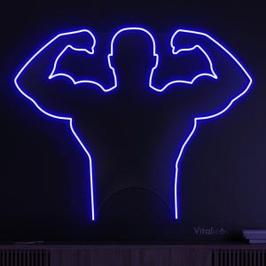 May include: A blue neon sign in the shape of a muscular person flexing their biceps. The sign is mounted on a dark wall above a wooden cabinet. The sign is a vibrant blue color.