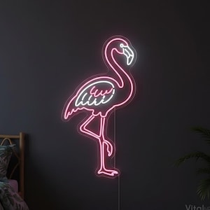 May include: A neon flamingo sign with a pink outline and white inner details is mounted on a dark gray wall. The sign is lit, showcasing the bird's silhouette. The sign is a decorative element.
