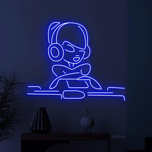 May include: Blue neon sign depicting a cartoon person wearing headphones and sitting in front of a computer. The sign is mounted on a wall.
