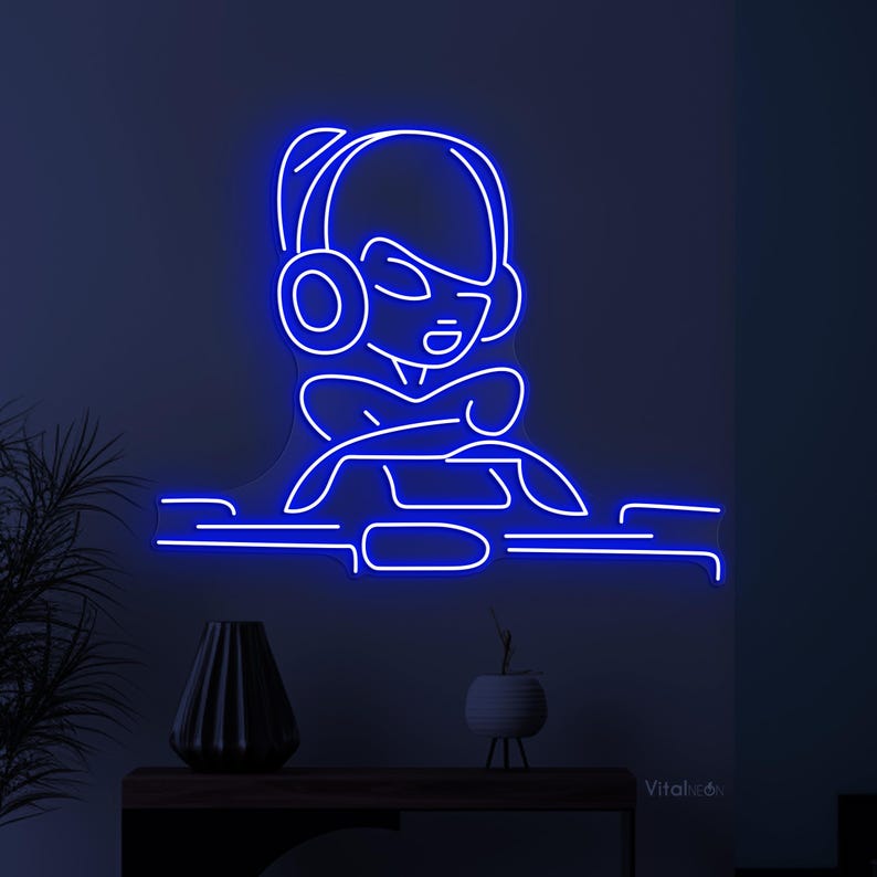May include: Blue neon sign depicting a cartoon person wearing headphones and sitting in front of a computer. The sign is mounted on a wall.