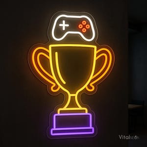 May include: A neon sign featuring a white gaming controller icon positioned above a yellow trophy cup with a purple base. The design is outlined in a dark border, creating a glowing effect against the wall. The text VitalNeon is visible in the corner.