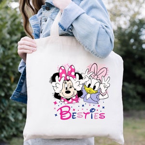 May include: A white canvas tote bag with a pink and purple design featuring Minnie Mouse and Daisy Duck. The design includes the word "Besties" in pink and purple letters.