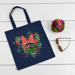 Puede incluir: Una bolsa de tela azul marino con un lazo rojo con lunares blancos y salpicaduras de pintura verde y blanca. El lazo tiene forma de cabeza de rat&oacute;n.