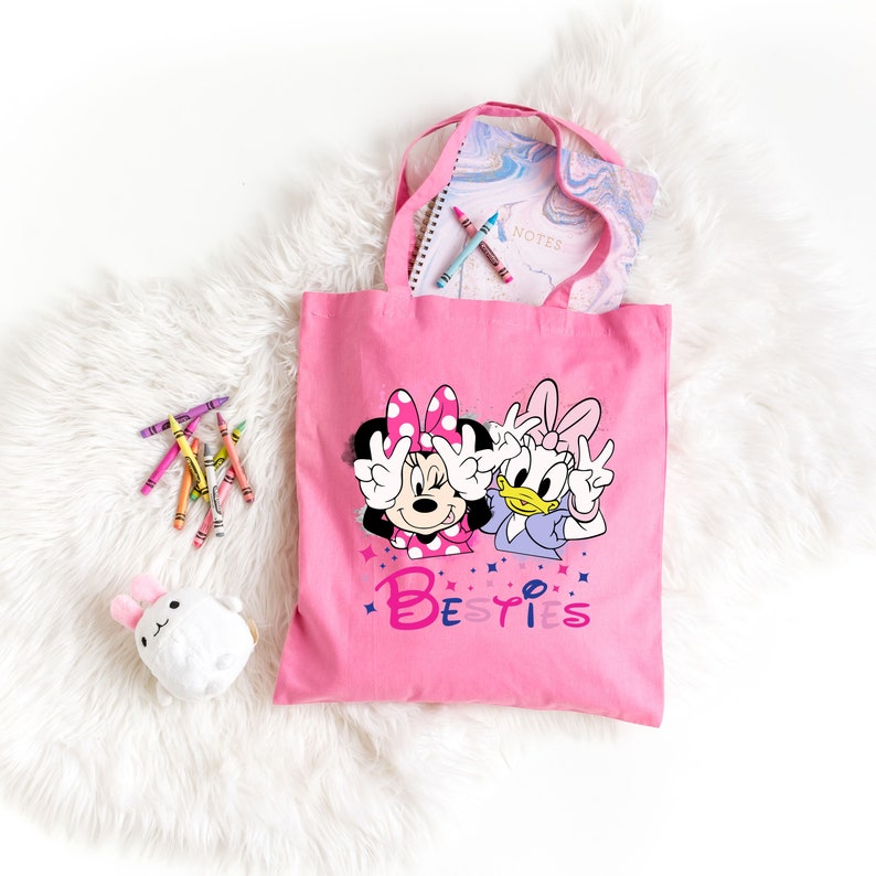 May include: Pink canvas tote bag featuring a graphic of Minnie Mouse and Daisy Duck with the text "Besties".