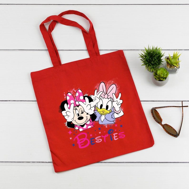 May include: Red canvas tote bag featuring a graphic of Minnie Mouse and Daisy Duck with the text "Besties".