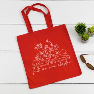 K&ouml;nnte beinhalten: Rote Einkaufstasche mit einer wei&szlig;en Umrandung eines Buches mit Blumen und dem Text "just one more chapter".