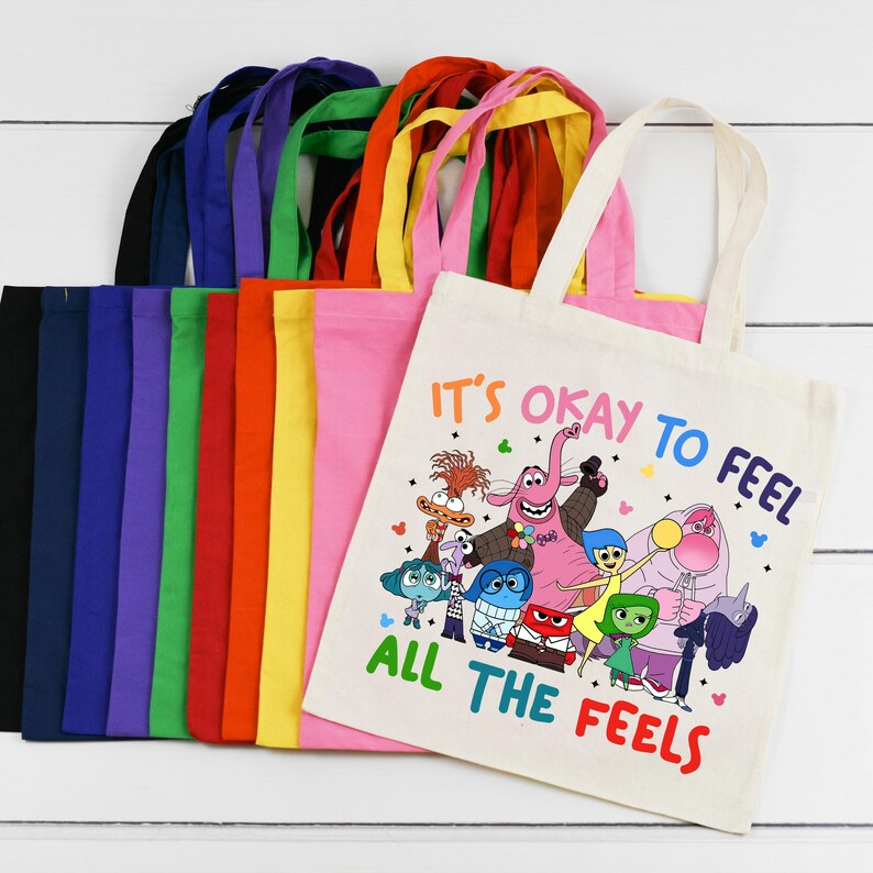 K&ouml;nnte beinhalten: Ein Set aus 10 bunten Tragetaschen mit einer wei&szlig;en Tragetasche, die eine Grafik der Figuren aus dem Film Inside Out zeigt. Die wei&szlig;e Tragetasche tr&auml;gt den Text "Es ist okay, alle Gef&uuml;hle zu f&uuml;hlen".
