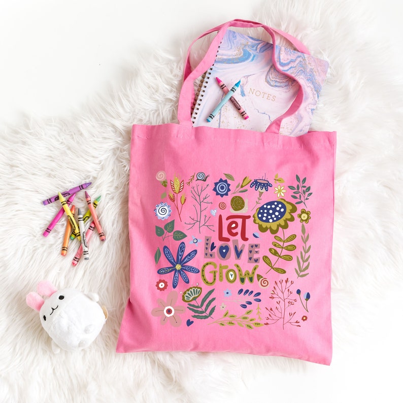May include: Pink canvas tote bag with a floral design and the text "Let Love Grow".